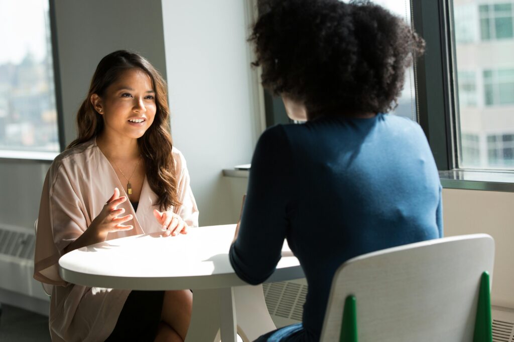 pexels photo 1181715 1181715 Two women sitting at a table having a professional discussion in a bright office setting.