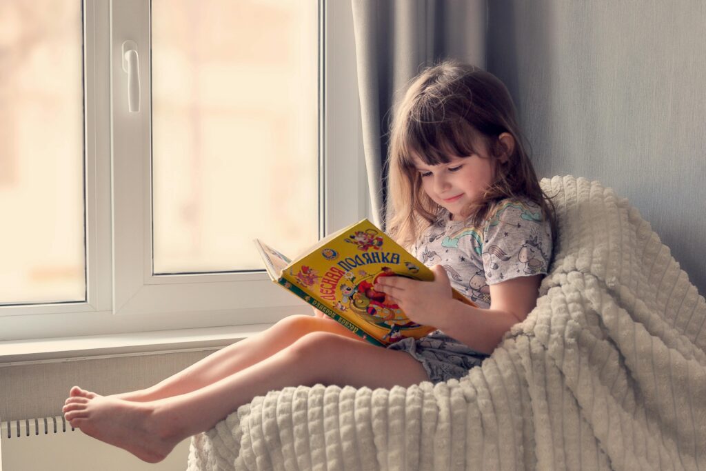 pexels photo 11065349 11065349 A young girl reads a colorful book by the window, embracing cozy and peaceful leisure time indoors.